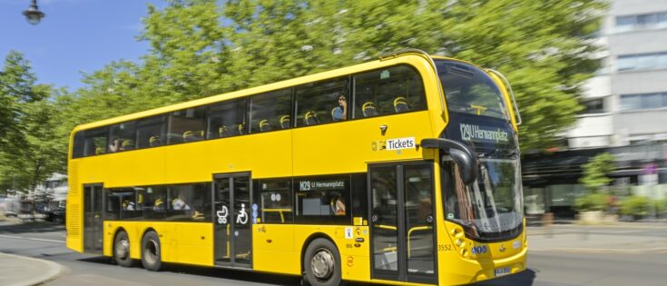 Gelber Doppeldeckerbus M 29 fährt auf dem Kurfürstendamm in Charlottenburg, Berlin, umgeben von grünen Bäumen.