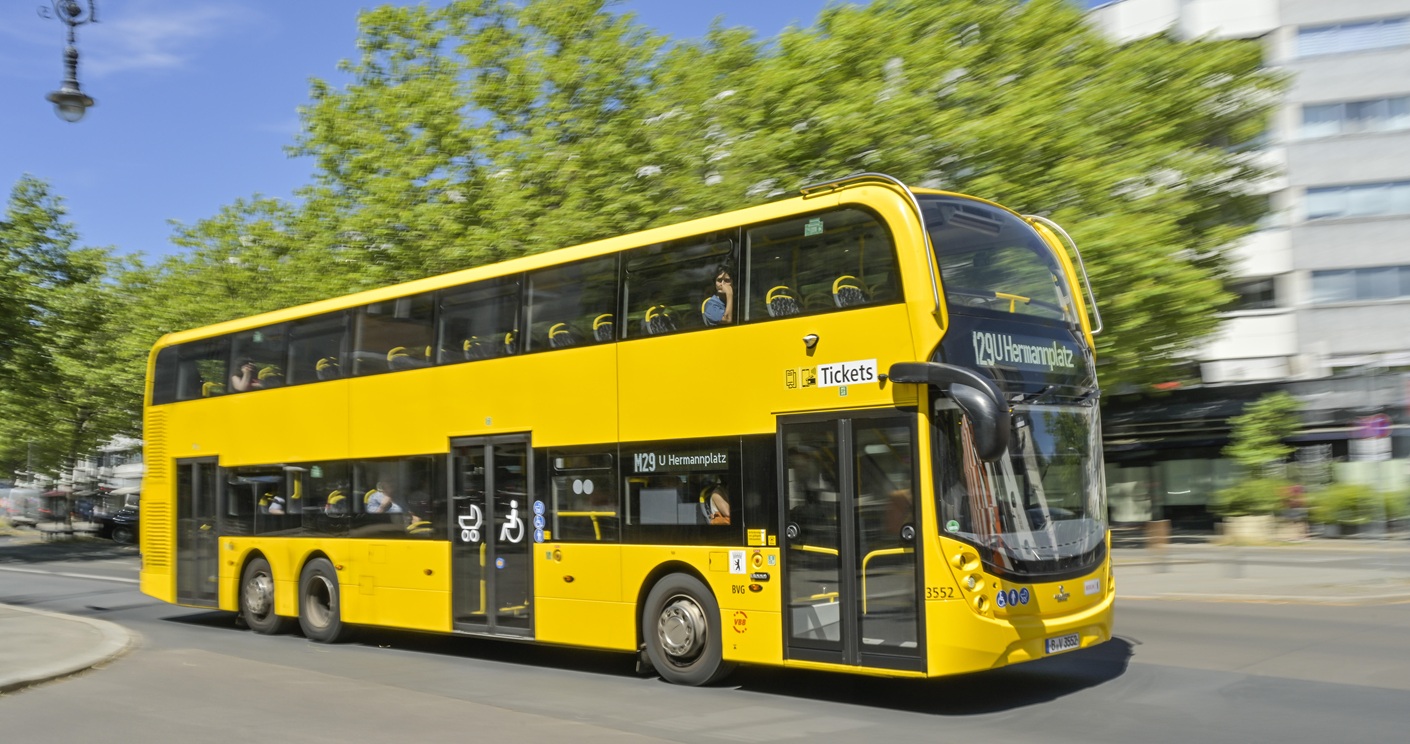 Gelber Doppeldeckerbus M 29 fährt auf dem Kurfürstendamm in Charlottenburg, Berlin, umgeben von grünen Bäumen.