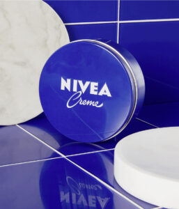 NIVEA Creme Dose auf blauer Fliese, umgeben von runden, weißen und marmorierten Objekten.