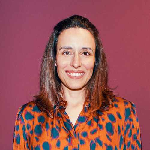 Porträt von Laurence Trillig mit braunen Haaren und einem orange-blauen Leopardenmusterhemd vor einem lila Hintergrund.