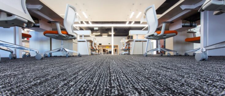 Bodenansicht eines modernen Büros mit Teppich und Büromöbeln, darunter Stühle mit Rollen und Schreibtische.