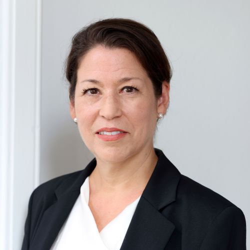 Porträt von Miriam Holbe-Finkelnburg in einem schwarzen Blazer vor einer hellen Wand.